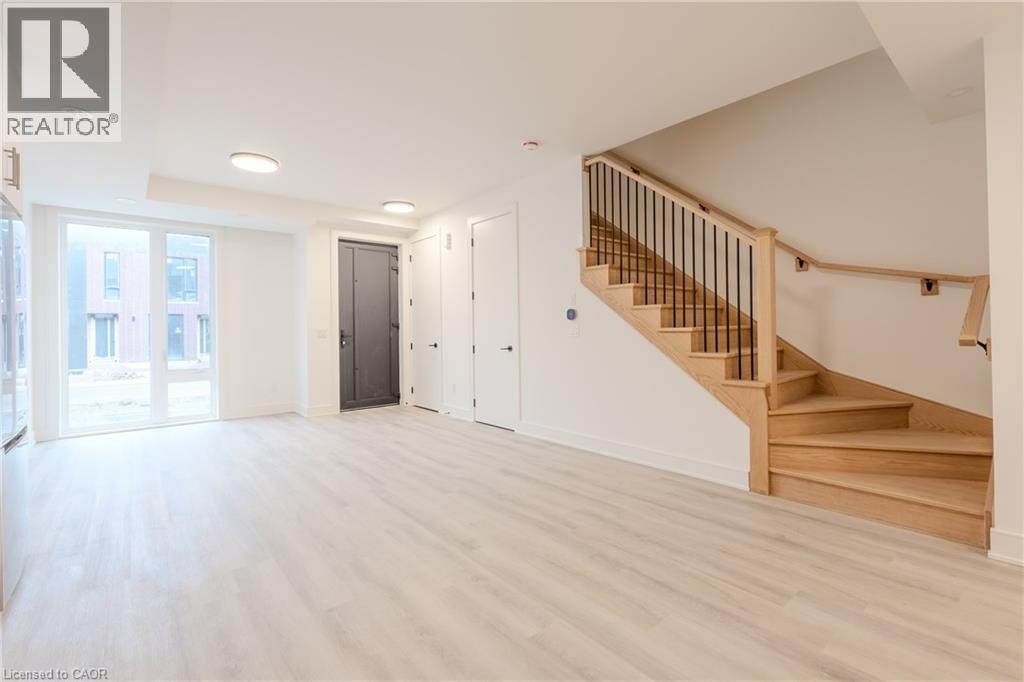 The property features light-colored flooring, a wooden staircase with black iron balusters, and a large glass door providing natural light - 144 Everett Common, St. Catharines, ON - Indoor Photo Showing Other Room