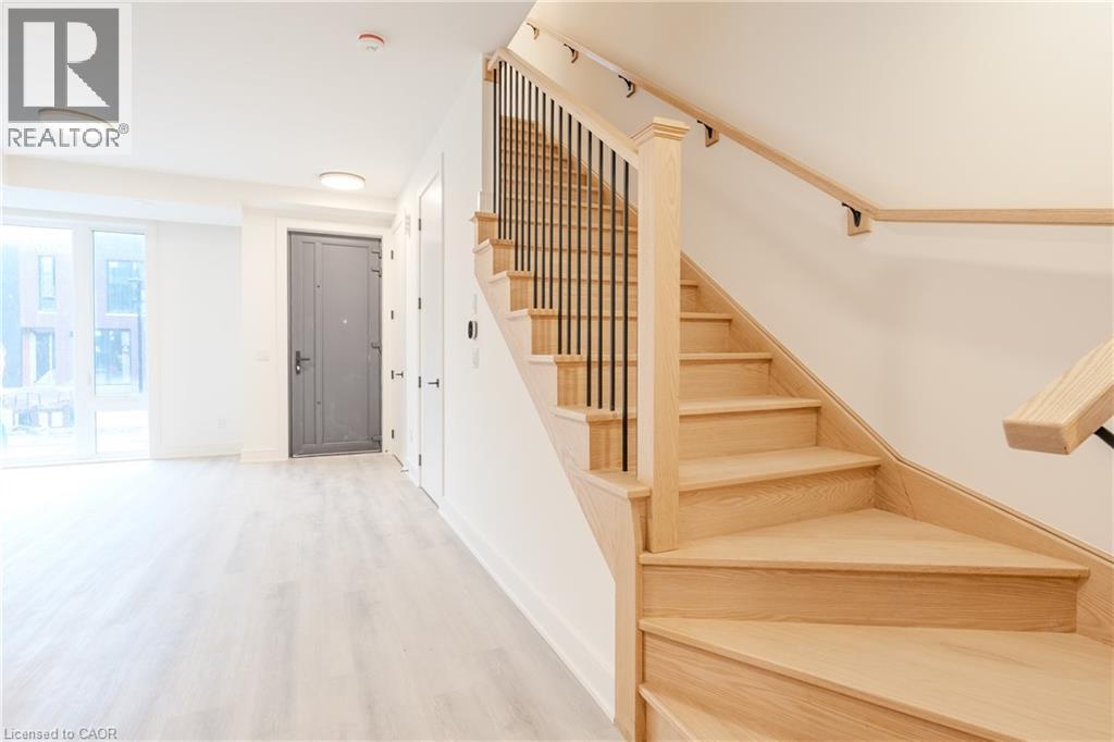 The entryway features light-colored flooring, a solid gray door, and a wooden staircase with black iron balusters - 144 Everett Common, St. Catharines, ON - Indoor Photo Showing Other Room