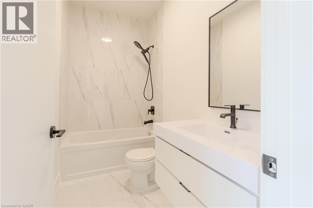 The bathroom features a white bathtub with a shower, a modern vanity with an integrated sink, and matte black fixtures - 144 Everett Common, St. Catharines, ON - Indoor Photo Showing Bathroom
