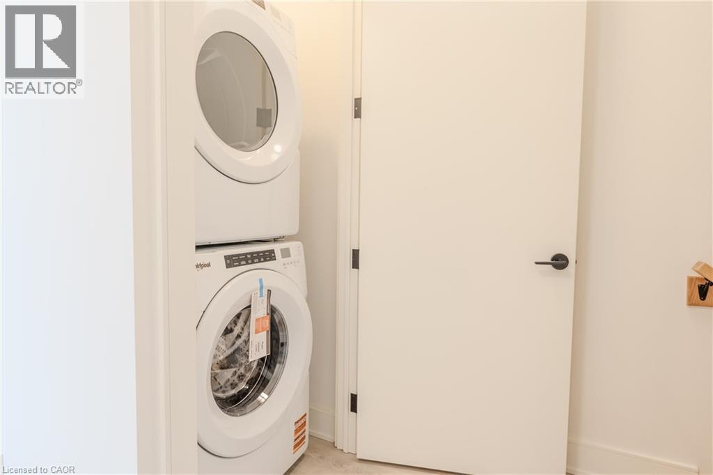 Convenient in-unit laundry with a stacked washer and dryer set, complemented by a white door with a matte black handle - 144 Everett Common, St. Catharines, ON - Indoor Photo Showing Laundry Room