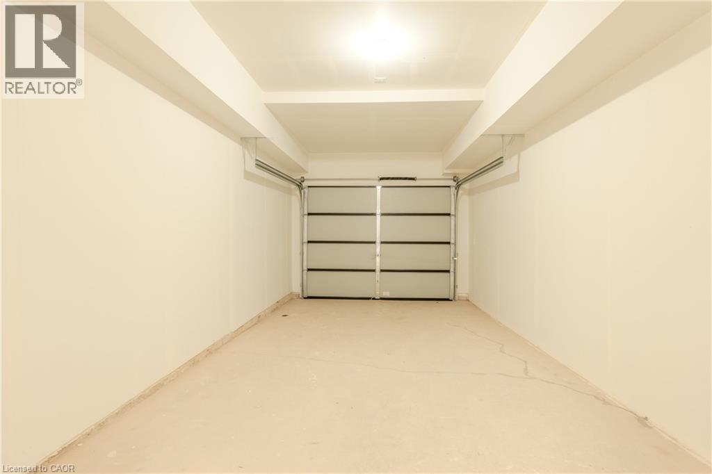 The property features a garage with a roll-up door, overhead lighting, and concrete flooring - 144 Everett Common, St. Catharines, ON - Indoor Photo Showing Garage