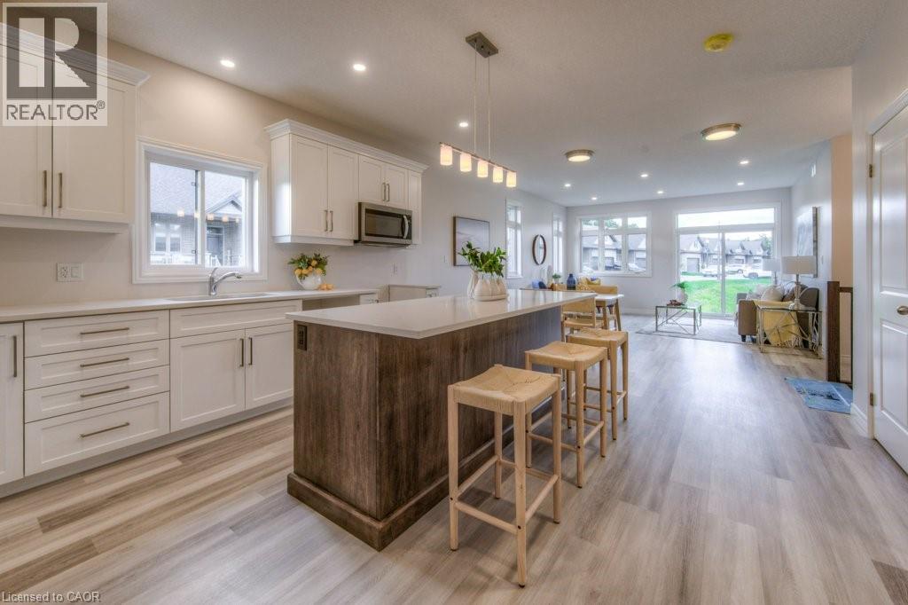 Open-concept living space featuring a central kitchen island with seating, light wood-finish flooring, white cabinetry, recessed lighting, and expansive windows - 48 Main Street E, Innerkip, ON - Indoor Photo Showing Kitchen With Upgraded Kitchen
