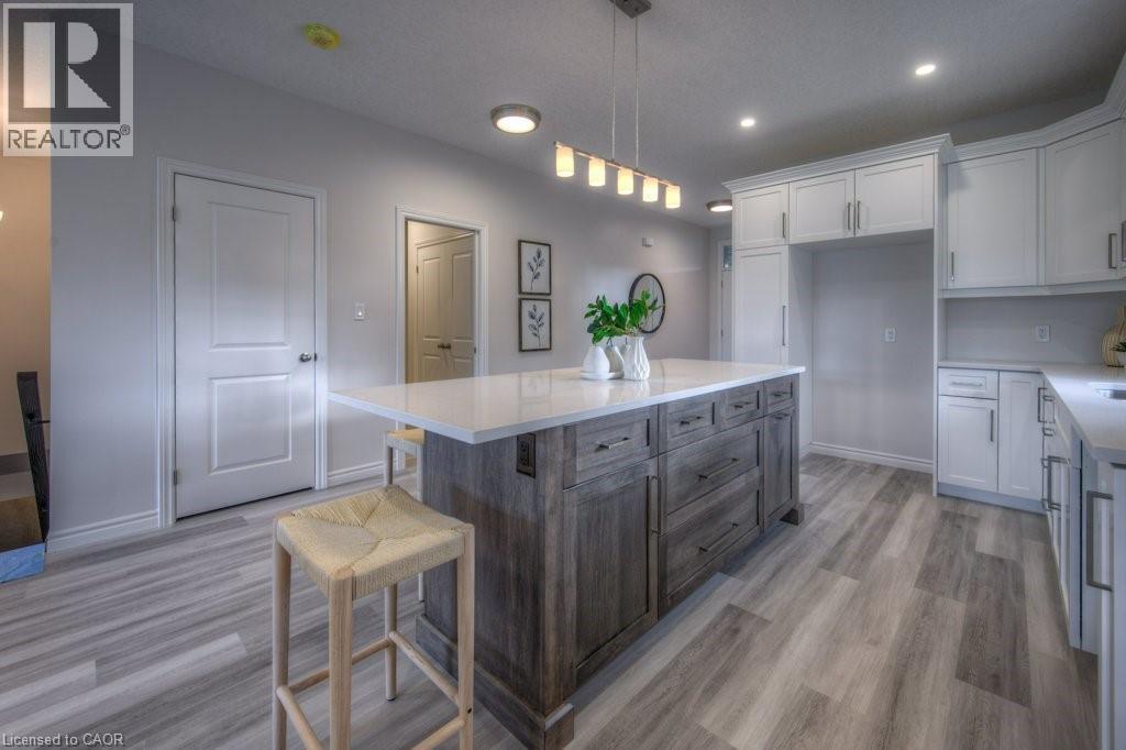Open-concept kitchen featuring a large central island with a solid surface countertop, wood-finish flooring, recessed lighting, white cabinetry, and a built-in refrigerator enclosure - 48 Main Street E, Innerkip, ON - Indoor Photo Showing Kitchen