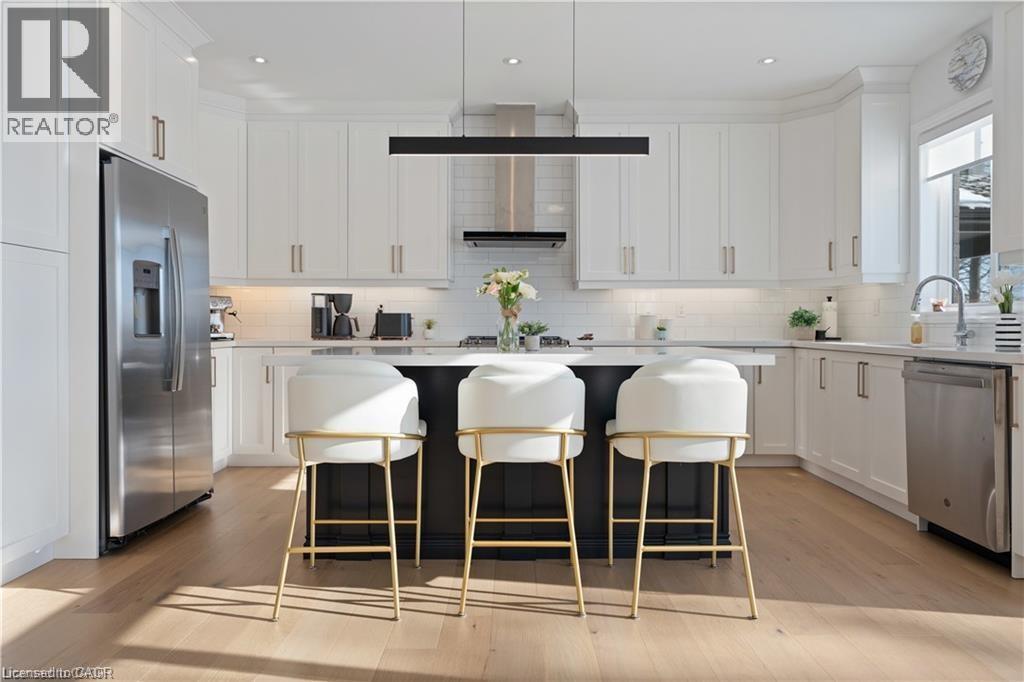 Kitchen with stainless steel appliances, light wood-style floors, white cabinets, a kitchen breakfast bar, and ventilation hood - 66 Cesar Place, Ancaster, ON - Indoor Photo Showing Kitchen With Upgraded Kitchen
