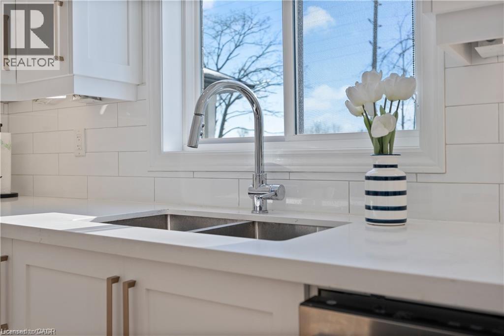 Kitchen featuring white cabinetry, light stone counters, stainless steel dishwasher, and decorative backsplash - 66 Cesar Place, Ancaster, ON - Indoor Photo Showing Kitchen With Double Sink
