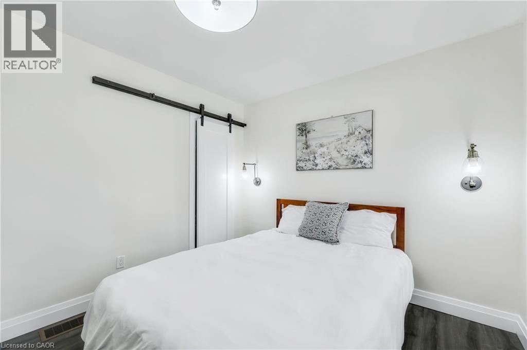 Bedroom featuring a white barn door, recessed ceiling light, wall-mounted sconce lighting, and dark wood-finish flooring - 18 Tweedsmuir Avenue, London, ON - Indoor Photo Showing Bedroom
