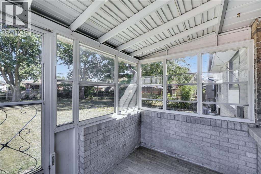 Enclosed patio featuring a corrugated metal roof, brick half-walls, and wood-finish flooring - 18 Tweedsmuir Avenue, London, ON - Photo Showing Other Room
