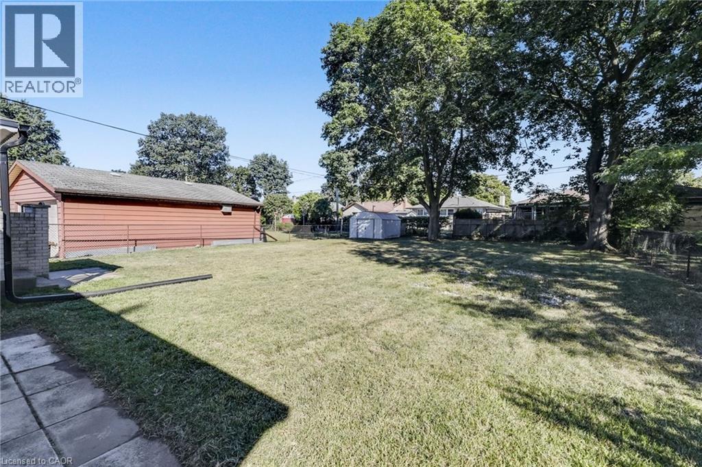Spacious backyard with a large grassy area, mature trees, a detached red-sided structure, and a perimeter fence - 18 Tweedsmuir Avenue, London, ON - Outdoor