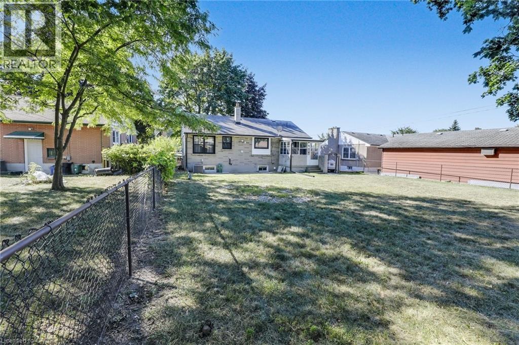Expansive backyard featuring a chain-link fence, mature trees, and a brick exterior home with multiple windows - 18 Tweedsmuir Avenue, London, ON - Outdoor