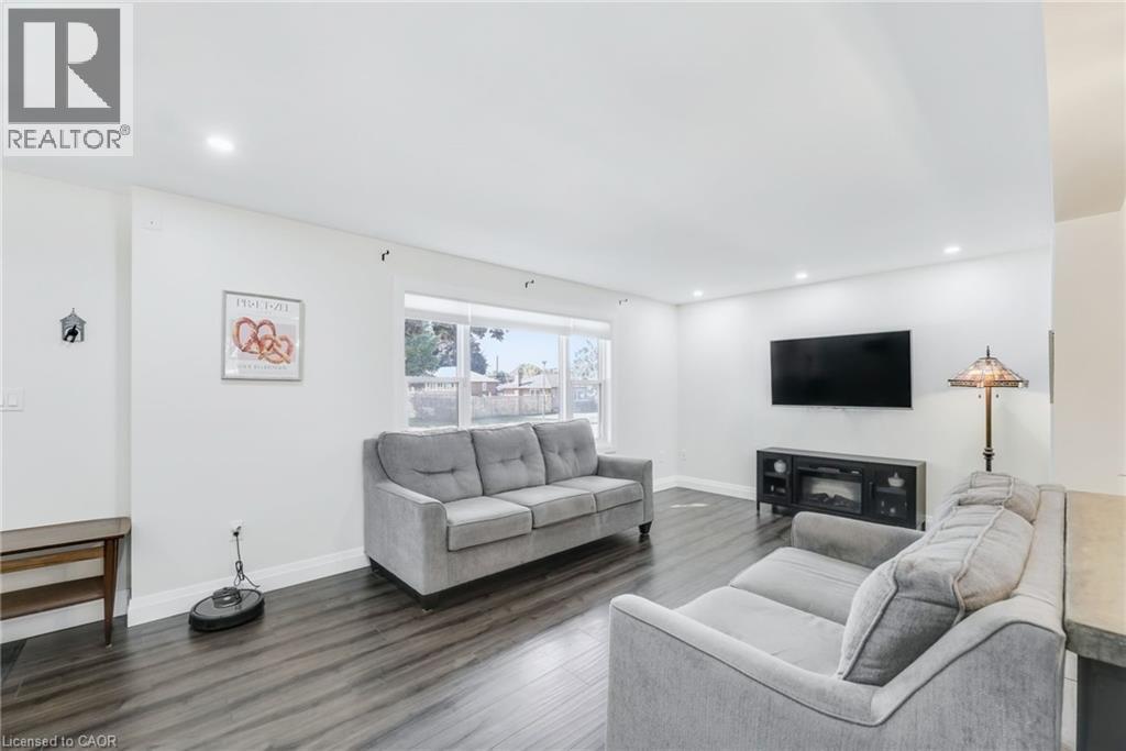 Spacious living area featuring wood-finish flooring, recessed lighting, a large window, and a media console with an electric fireplace - 18 Tweedsmuir Avenue, London, ON - Indoor Photo Showing Living Room With Fireplace