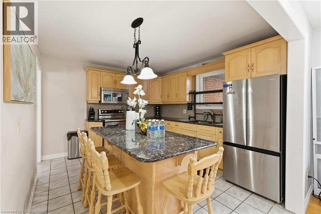 Kitchen with appliances with stainless steel finishes, dark stone counters, pendant lighting, light brown cabinetry, and a kitchen island - 364 Roselawn Place, Waterloo, ON - Indoor