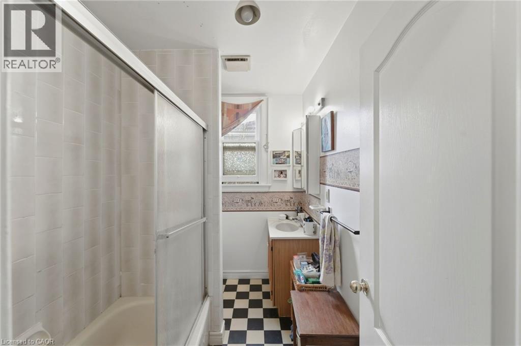 Bathroom featuring a tub/shower combination with sliding glass doors, white tiled walls, and a checkerboard floor - 509 Aberdeen Avenue, Hamilton, ON - Indoor Photo Showing Bathroom