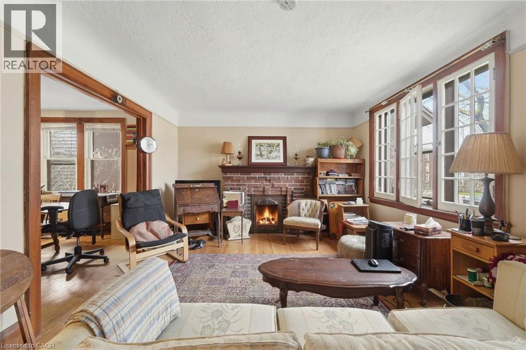 Living room featuring wood-finish flooring, a brick fireplace with a wood mantle, and white-framed windows with dark wood trim - 509 Aberdeen Avenue, Hamilton, ON - Indoor Photo Showing Living Room With Fireplace