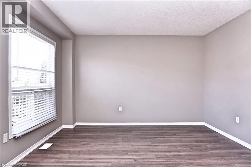 Spacious room featuring wood-finish flooring, neutral-toned walls, and a large window with white blinds - 40 Madeleine Street, Kitchener, ON