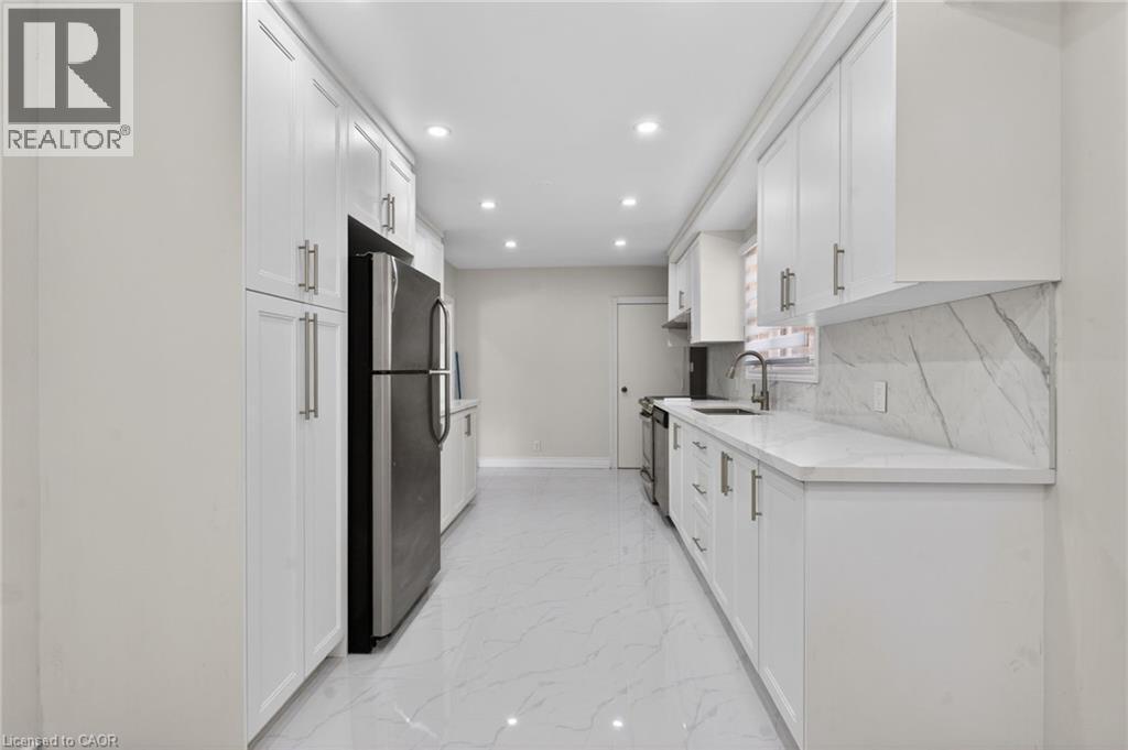 Galley kitchen featuring extensive white cabinetry with brushed nickel hardware, a stainless steel refrigerator, and a matching range - 53 Nicklin Crescent, Guelph, ON - Indoor Photo Showing Kitchen