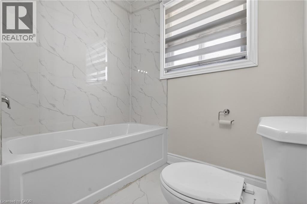 Bathroom featuring a white soaking tub with polished chrome fixtures, white marbled tile surround, and a white toilet - 53 Nicklin Crescent, Guelph, ON - Indoor Photo Showing Bathroom