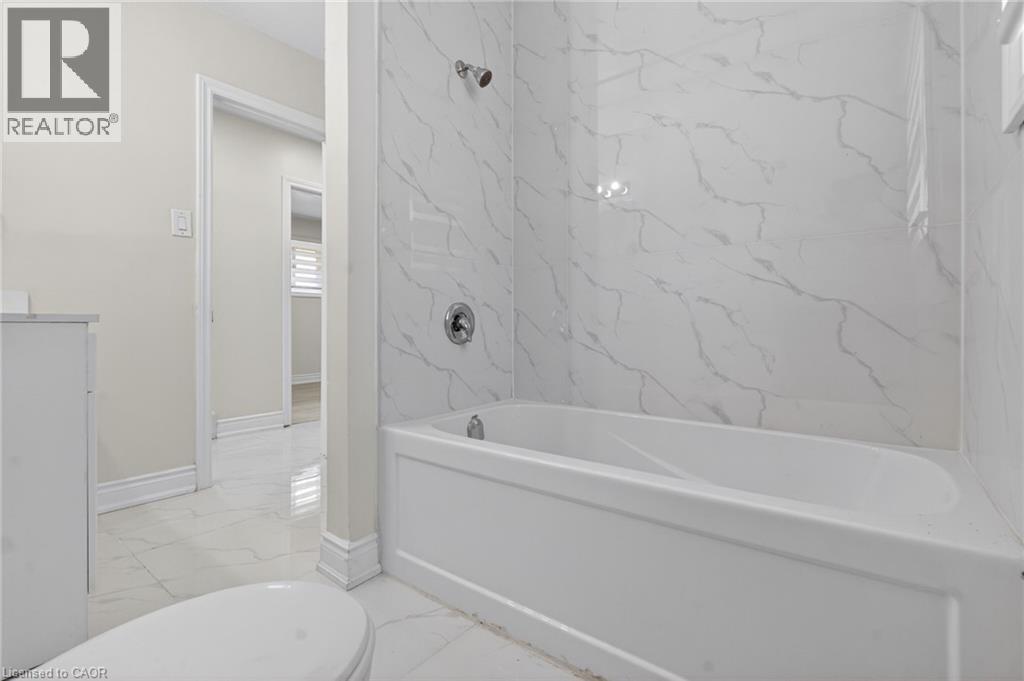 Bathroom featuring a white porcelain bathtub with chrome fixtures, surrounded by large format white tiles with subtle grey veining - 53 Nicklin Crescent, Guelph, ON - Indoor Photo Showing Bathroom