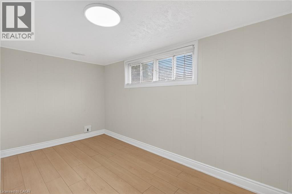 Room featuring wood-finish flooring, a window with horizontal blinds, light-toned wall paneling, white baseboards, and a flush-mount ceiling light fixture - 53 Nicklin Crescent, Guelph, ON - Indoor Photo Showing Other Room