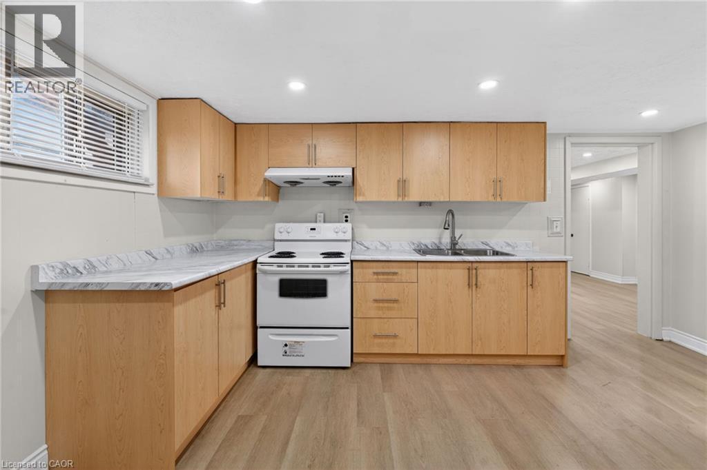 Kitchen featuring L-shaped wood-finish cabinetry with brushed nickel hardware, light-toned countertops, a white electric range, and a stainless steel sink with a high-arc faucet - 53 Nicklin Crescent, Guelph, ON - Indoor Photo Showing Kitchen With Double Sink