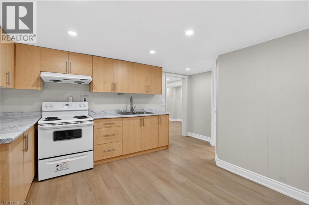 Kitchen featuring wood-finish cabinetry, light-toned countertops, and a white electric range with overhead ventilation - 53 Nicklin Crescent, Guelph, ON - Indoor Photo Showing Kitchen With Double Sink