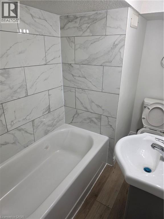 Bathroom featuring a white bathtub with white marbled tile surround and a pedestal sink - 22 Montrose Avenue, Kitchener, ON - Indoor Photo Showing Bathroom