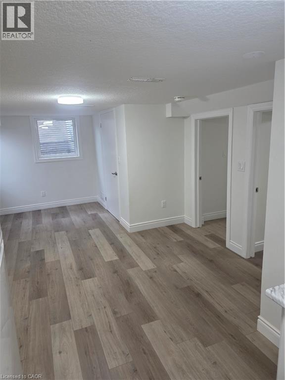 Spacious room featuring wood-finish flooring, white baseboards, and a large egress window - 22 Montrose Avenue, Kitchener, ON - Indoor Photo Showing Other Room