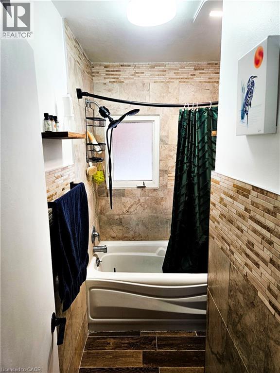 Bathroom featuring a white tub with a curved apron, stone-look wall tiles, a mosaic tile accent band, a frosted window, and wood-finish floor tiles - 34 Christopher Drive, Cambridge, ON - Indoor Photo Showing Other Room