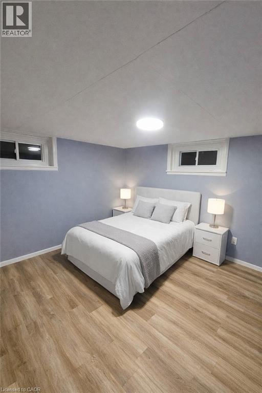 Wood-finish flooring throughout, featuring a light blue wall finish, two recessed windows with white trim, and overhead flush-mount lighting - 34 Christopher Drive, Cambridge, ON - Indoor Photo Showing Bedroom