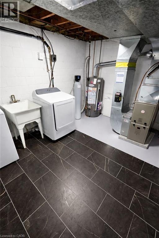 Utility area featuring dark rectangular tile flooring, white block walls, exposed ceiling joists, and a white utility sink - 34 Christopher Drive, Cambridge, ON - Indoor