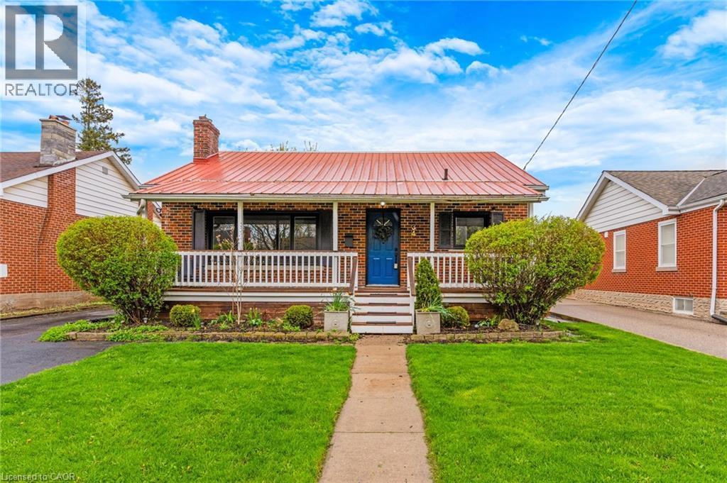 Brick exterior featuring a bright red metal roof, covered front porch, and a vibrant blue entry door - 34 Christopher Drive, Cambridge, ON - Outdoor With Deck Patio Veranda