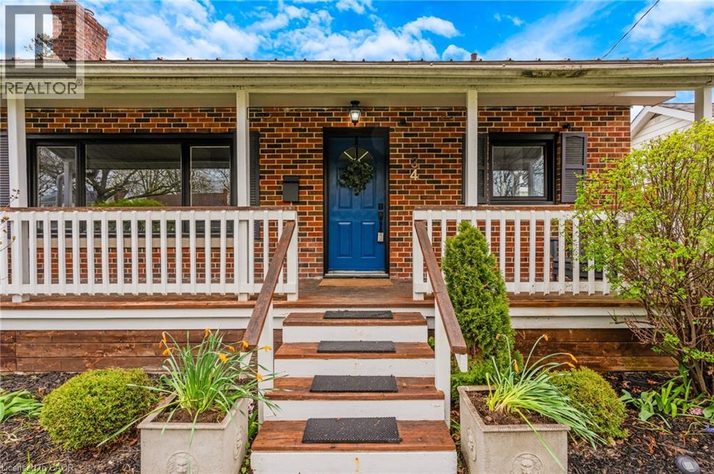 Brick exterior featuring a covered front porch with white railing, wood-finish stairs, and a prominent blue entry door - 34 Christopher Drive, Cambridge, ON - Outdoor With Deck Patio Veranda