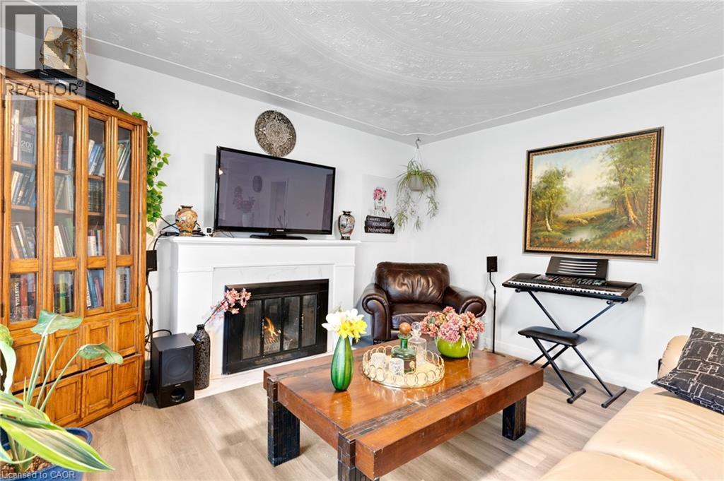 Living area featuring a white mantel fireplace with a dark firebox, wood-finish flooring, and a built-in wood display cabinet - 34 Christopher Drive, Cambridge, ON - Indoor Photo Showing Living Room With Fireplace