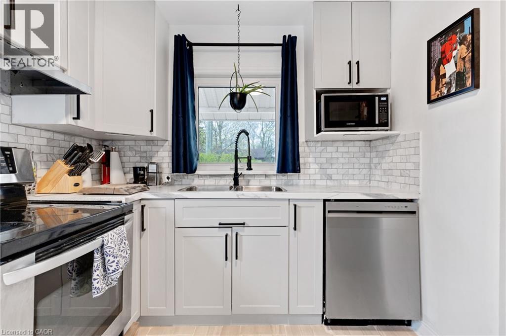 Modern kitchen featuring white shaker cabinetry with black hardware, subway tile backsplash, stainless steel appliances, and a double basin sink with a gooseneck faucet - 34 Christopher Drive, Cambridge, ON - Indoor Photo Showing Kitchen With Double Sink With Upgraded Kitchen
