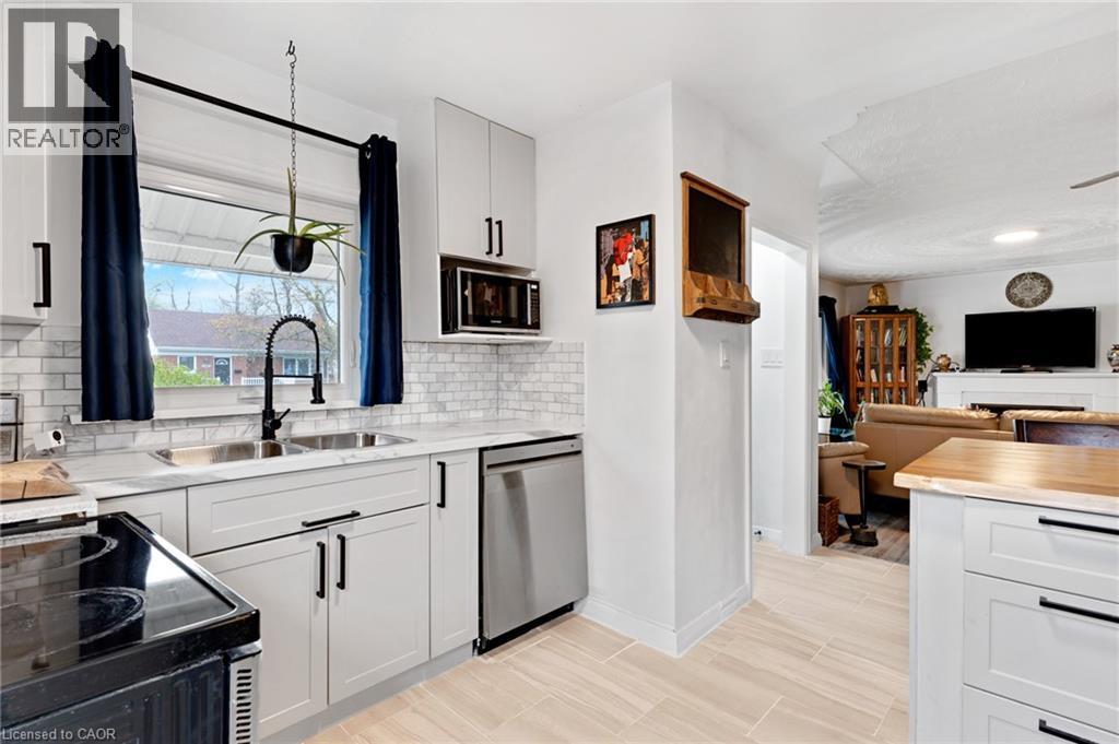 Modern kitchen featuring light gray cabinetry with black hardware, subway tile backsplash, stainless steel sink with gooseneck faucet, and integrated stainless steel dishwasher - 34 Christopher Drive, Cambridge, ON - Indoor Photo Showing Kitchen With Double Sink