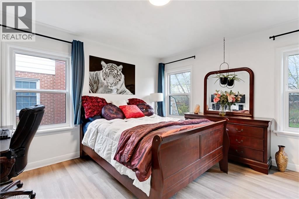 Bright bedroom featuring light wood-finish flooring, white walls, and multiple windows with dark curtain rods - 34 Christopher Drive, Cambridge, ON - Indoor Photo Showing Bedroom