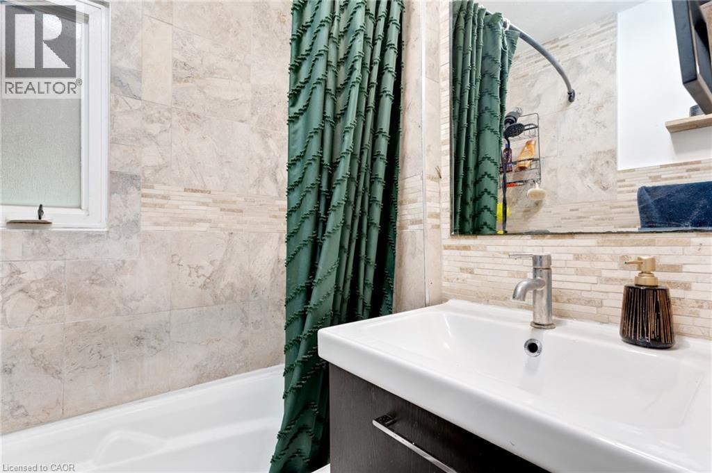 Bathroom featuring a white bathtub, frosted window, light-toned wall tiling, and a vanity with an integrated sink and chrome faucet - 34 Christopher Drive, Cambridge, ON - Indoor Photo Showing Bathroom