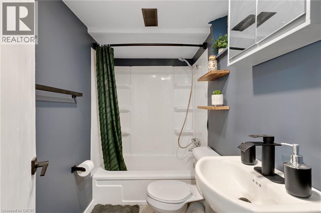 Compact bathroom featuring a white tub/shower combination, wall-mounted sink, and floating wood shelves - 34 Christopher Drive, Cambridge, ON - Indoor Photo Showing Bathroom