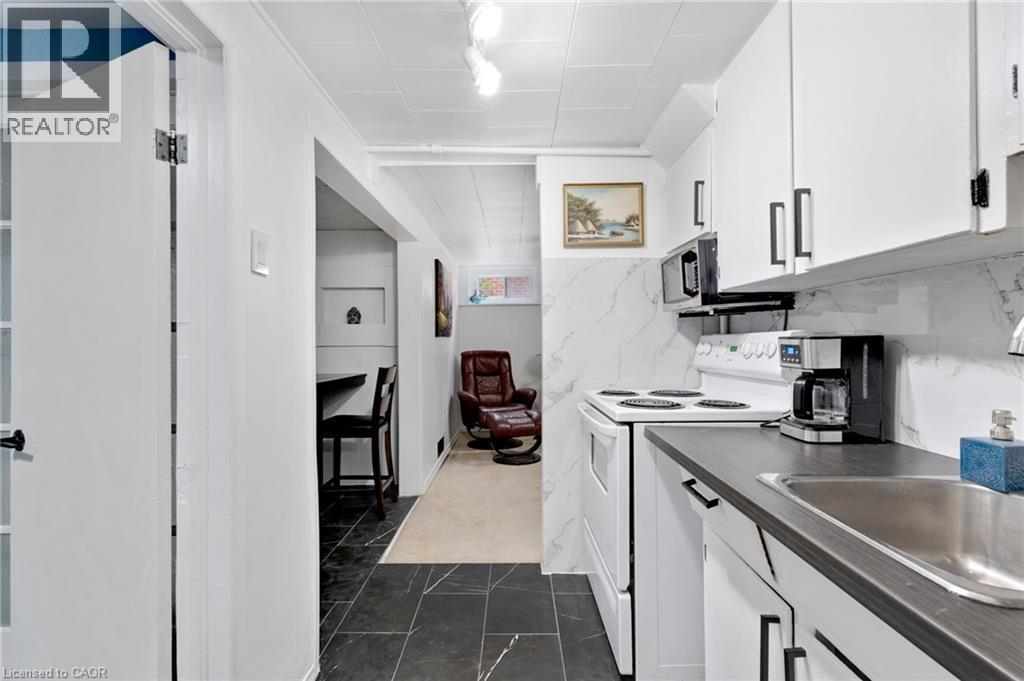 Compact kitchen featuring white cabinetry with dark hardware, dark countertops, white range, and built-in microwave - 34 Christopher Drive, Cambridge, ON - Indoor Photo Showing Kitchen