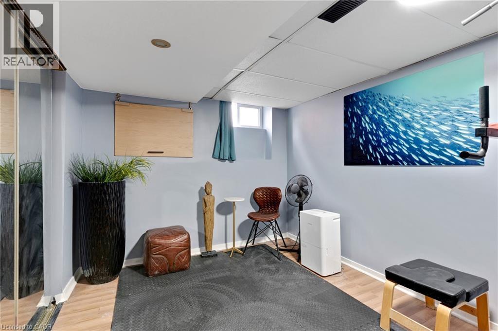 Recessed lighting illuminates this versatile space featuring wood-finish flooring, a wall-mounted display, and a large mirrored wall - 34 Christopher Drive, Cambridge, ON - Indoor Photo Showing Other Room