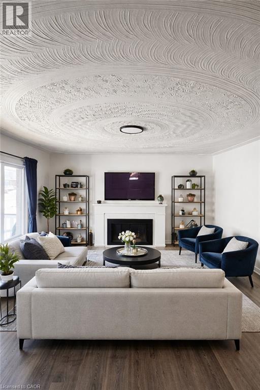 Living area featuring a textured ceiling with a central light fixture, a fireplace with a white mantel, and wood-finish flooring - 34 Christopher Drive, Cambridge, ON - Indoor Photo Showing Living Room With Fireplace