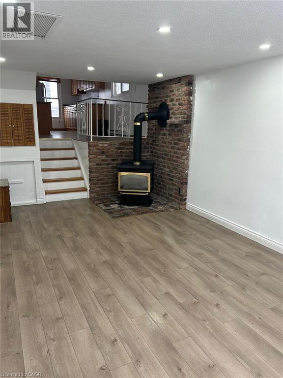 Spacious interior featuring wide plank wood-finish flooring, a brick accent wall with a wood-burning stove, recessed lighting, and a white metal staircase railing - 744 Parkview Crescent, Cambridge, ON - Indoor Photo Showing Other Room With Fireplace