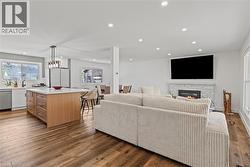 Open-concept living space featuring wood-finish flooring, recessed lighting, and a white stacked stone fireplace - 