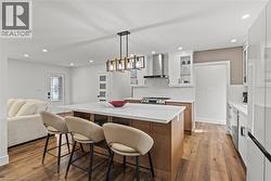 Kitchen featuring a large central island with seating, pendant lighting, stainless steel appliances, white cabinetry with glass inserts, and wood-finish flooring - 