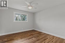 Room featuring wood-finish flooring, a ceiling fan with integrated lighting, a single window, white trim, and light gray walls - 