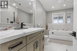 Full bathroom featuring a single vanity with a stone countertop, a built-in tub with tile surround, a window, and recessed lighting - 