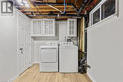 Dedicated laundry area featuring wood-finish flooring, white cabinetry with glass inserts, and a functional window - 