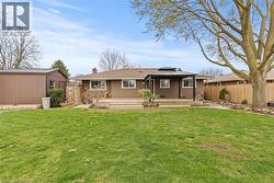 Expansive green lawn with a brown exterior home, featuring a large wooden deck, built-in black pergola, and a storage shed - 