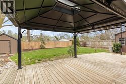 Expansive backyard featuring a large wooden deck, a covered gazebo, a manicured lawn, and a privacy fence - 