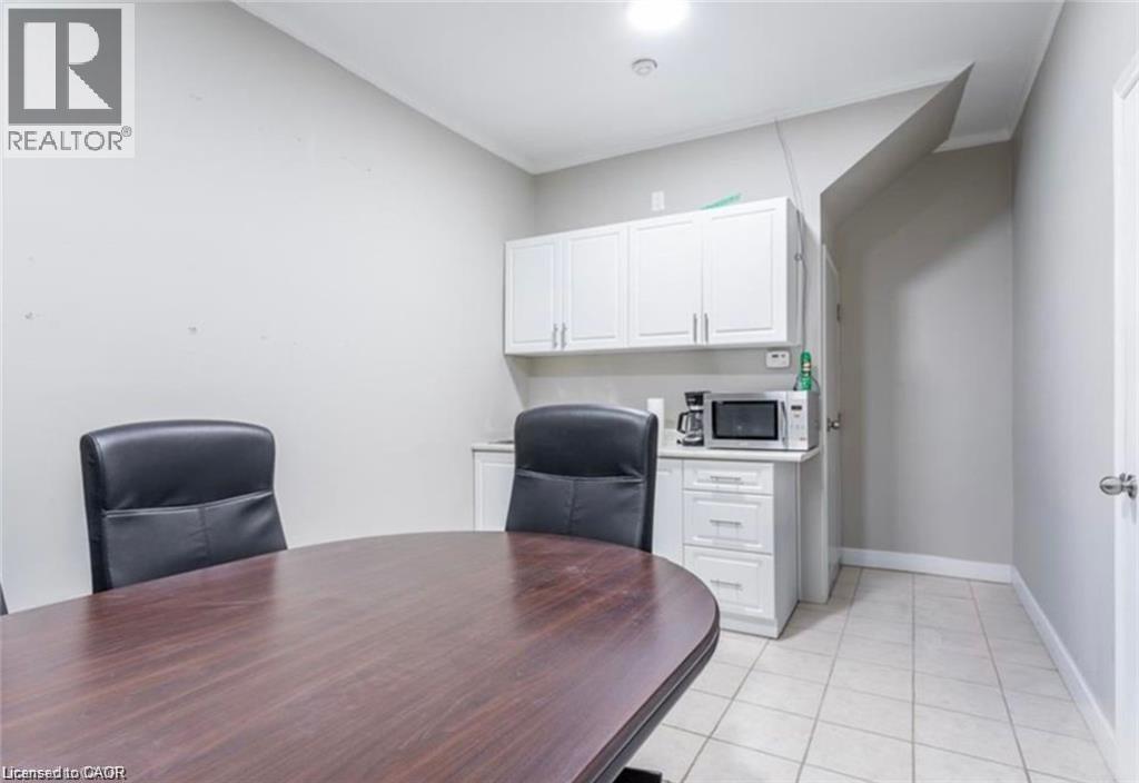 This room features a dark wood oval table, white upper and lower cabinetry, and light-toned floor tiles - 833 King Street E, Hamilton, ON