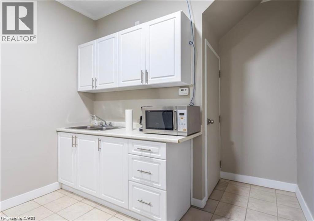 Utility space featuring white cabinetry with silver hardware, a stainless steel sink, and light-colored tiled flooring - 833 King Street E, Hamilton, ON